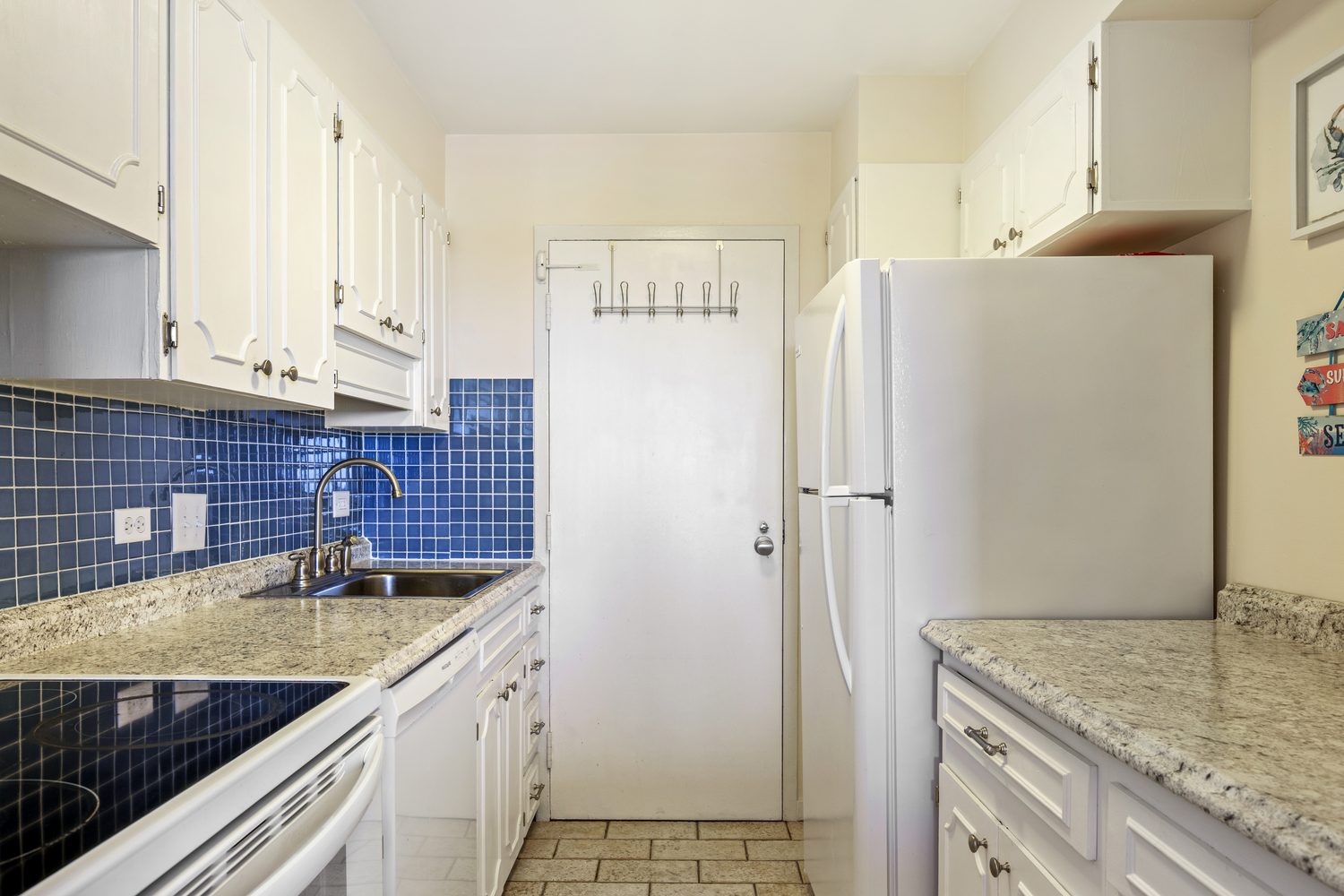 Galley kitchen with white cabinetry, granite counters, and cobalt tile backsplash